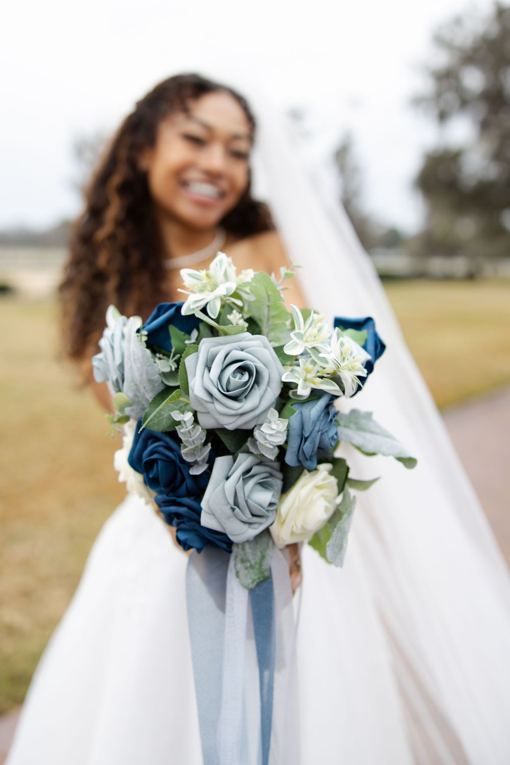 A stunning bridal bouquet features blue and silver roses with delicate greenery and ribbon.
