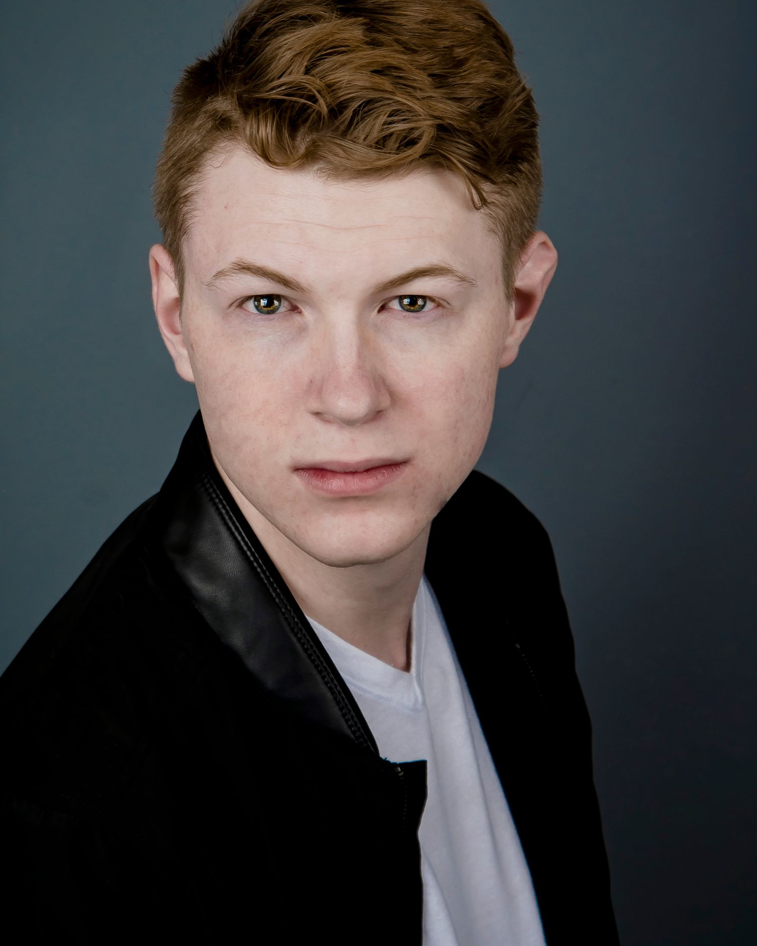 Professional headshot in black jacket against grey studio background.