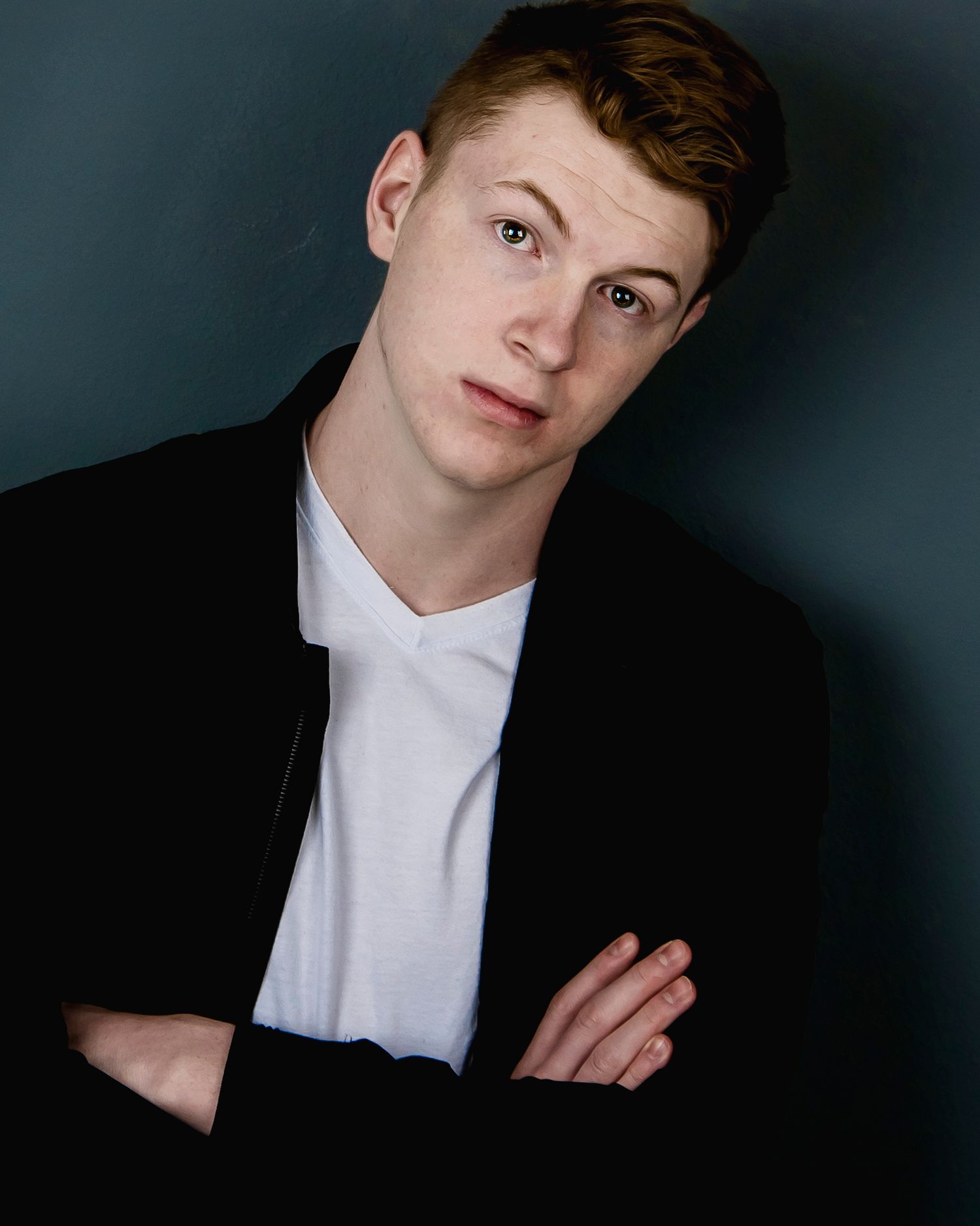 Studio portrait in black jacket and white shirt against dark background.