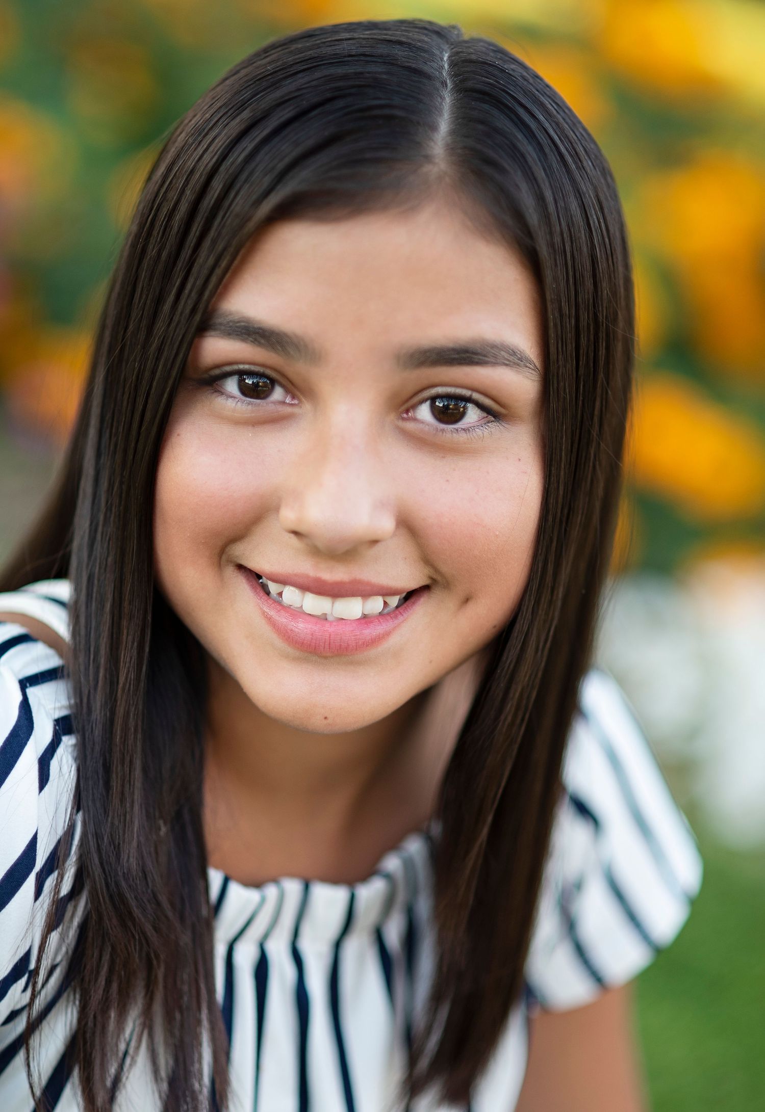 Portrait of person in striped blouse smiling outdoors with yellow flowers in background.
