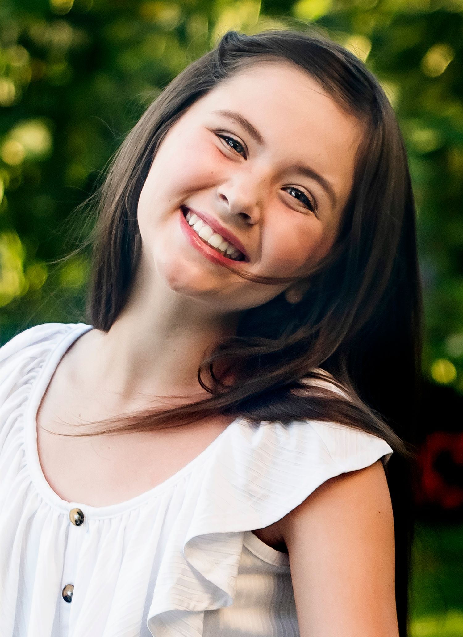 Cheerful outdoor portrait in white top with sunlit greenery background.
