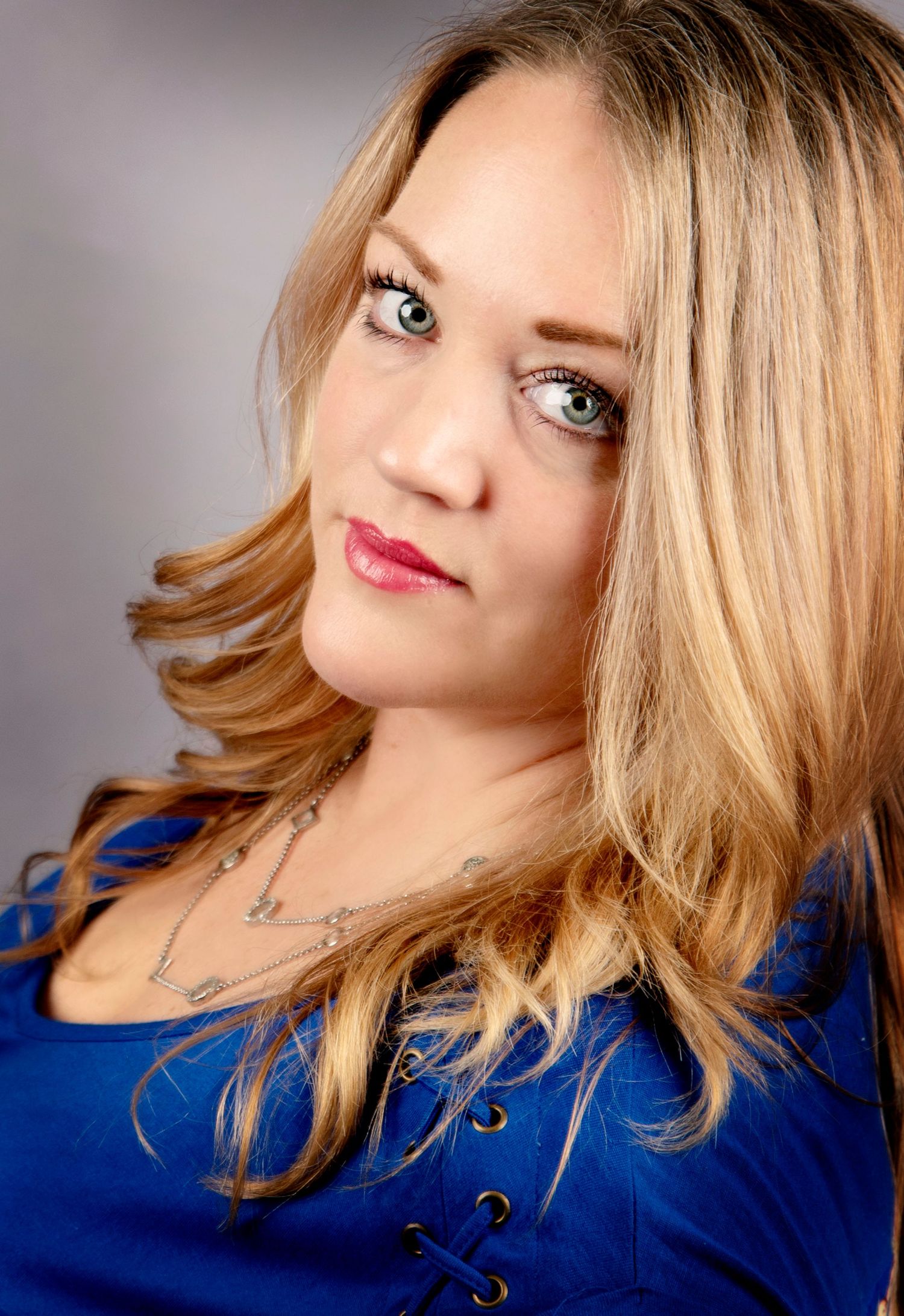 Portrait photo of someone with blonde wavy hair wearing a bright royal blue top against a neutral background.