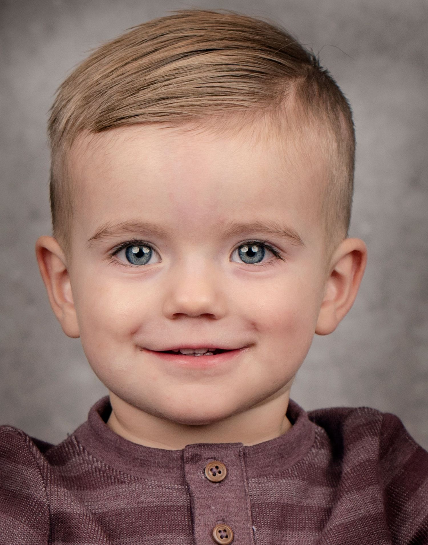 Studio portrait of toddler with bright blue eyes wearing brown henley shirt.