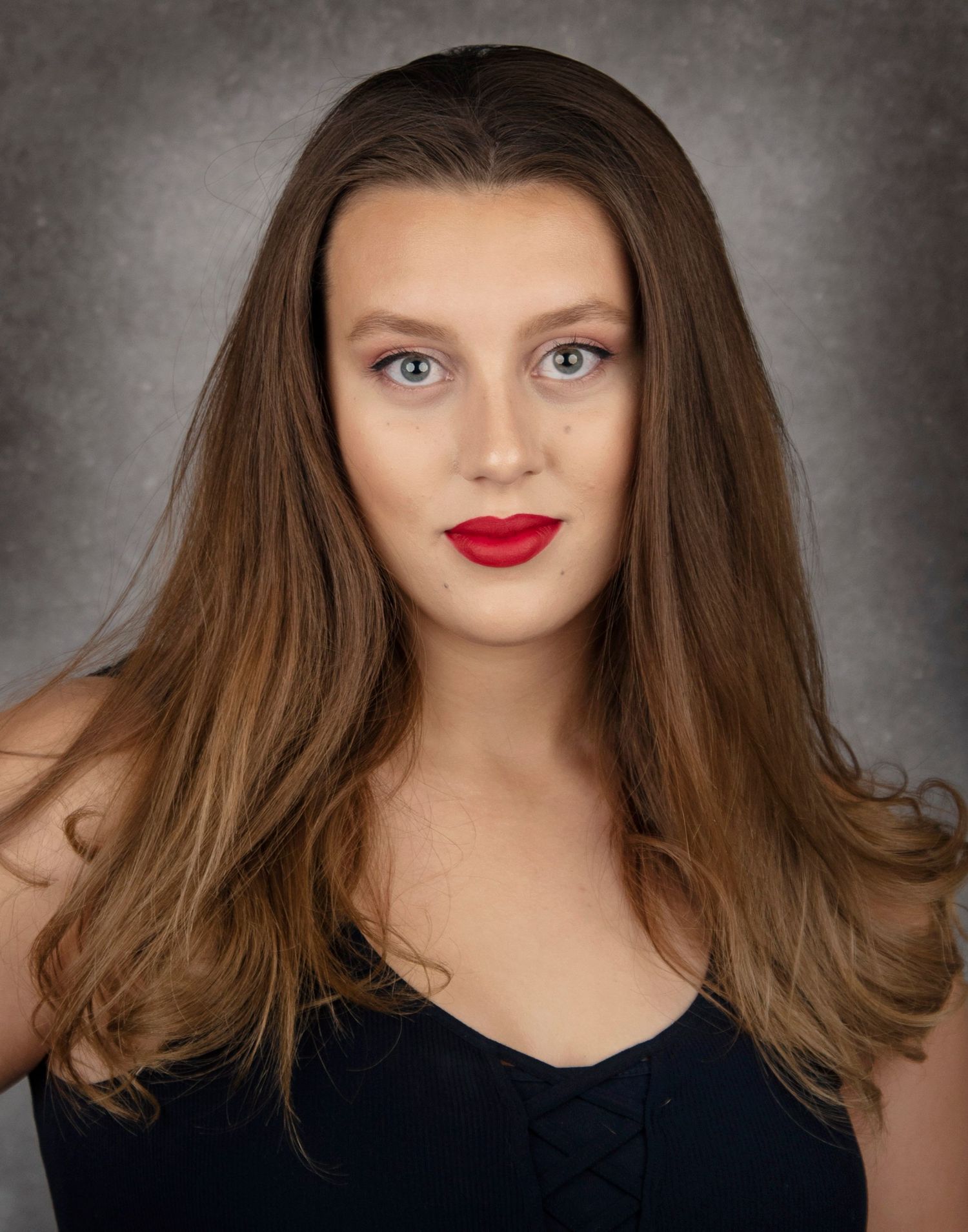 Studio portrait with neutral backdrop featuring glamorous makeup and ombre brown hair.