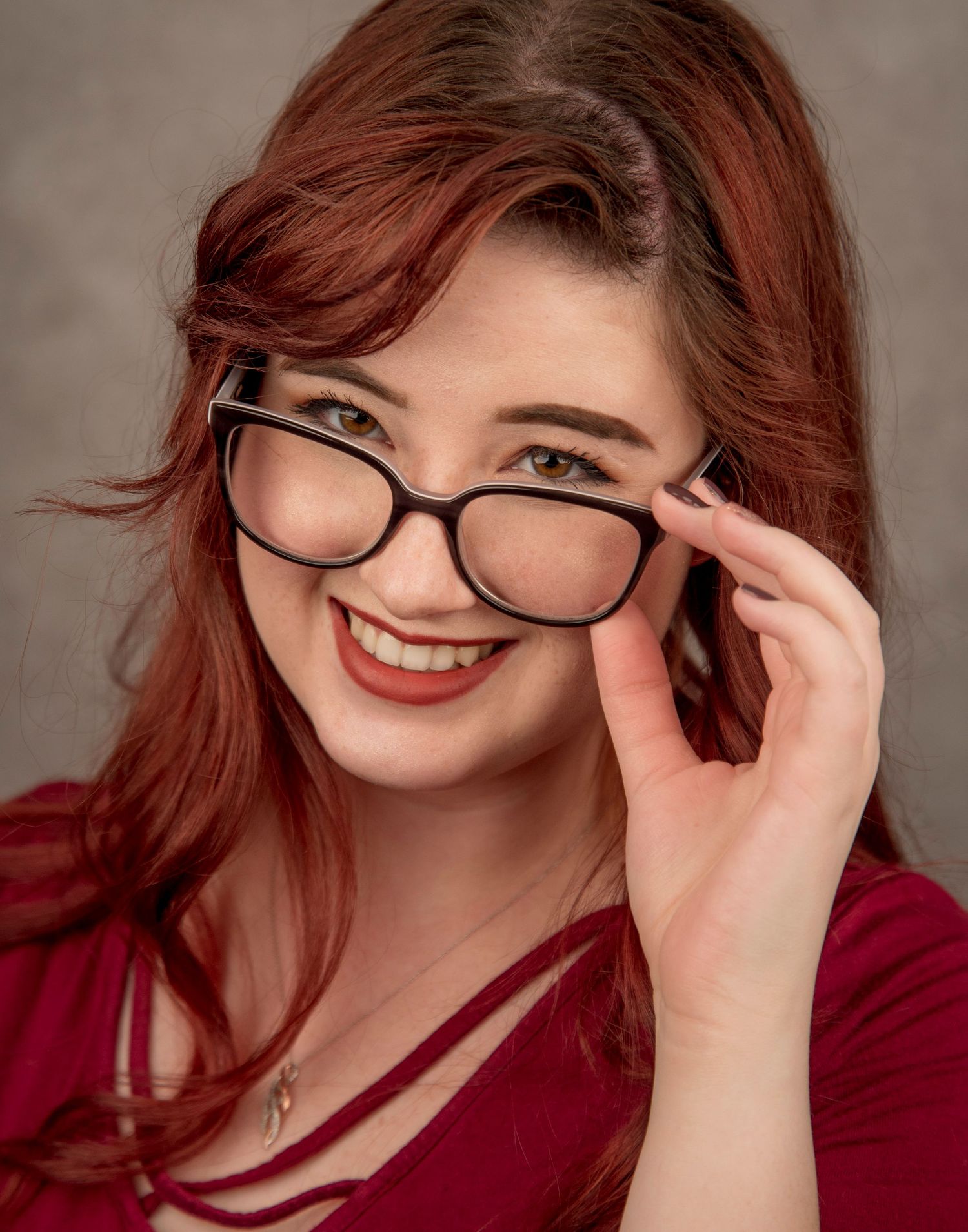 Portrait of someone wearing black-framed glasses and a red top, with vibrant auburn hair and a warm smile.