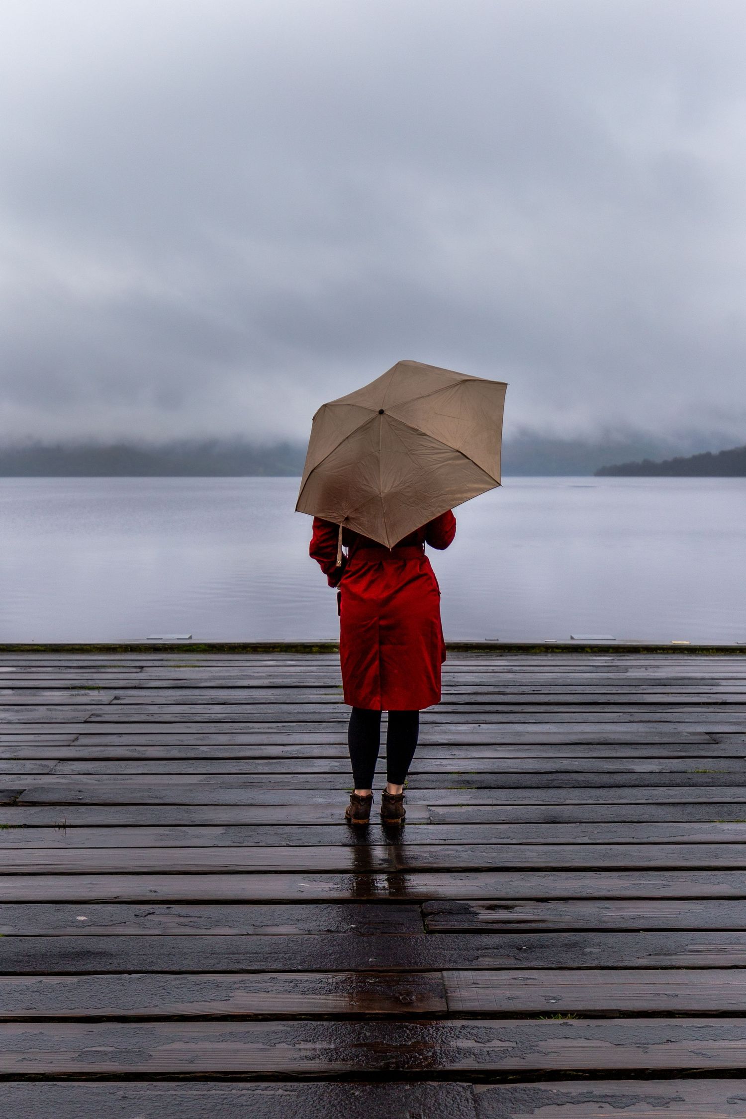 Travel Photographer taking a photo of a girl in a red jacket and Umbrella on Loch Luss in Scotland