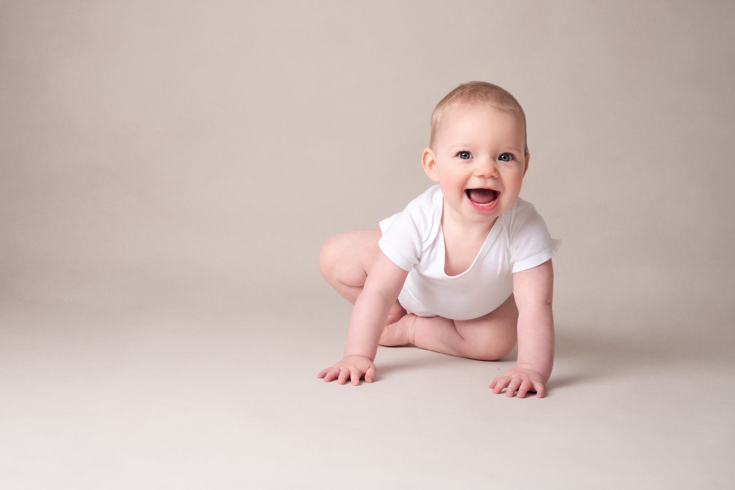 Happy crawling baby in white onesie on neutral studio background.