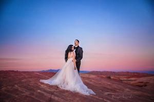 Wedding couple stands against vibrant desert sunset and red rock formations.