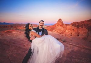 Joyful wedding couple embracing on red rock formations in the desert.