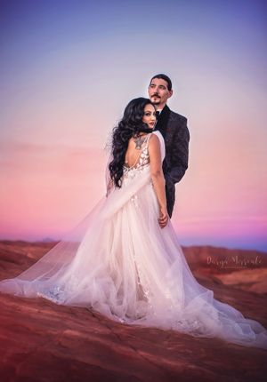 Desert wedding portrait with flowing white dress against purple sunset sky.