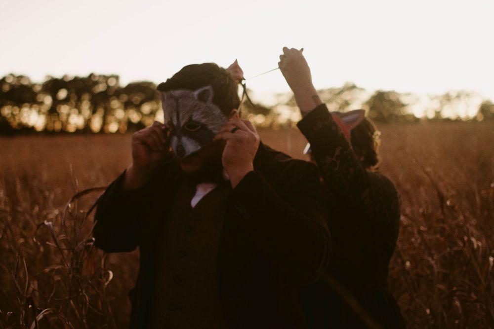 Two people in formal attire dance playfully in a golden field at sunset.