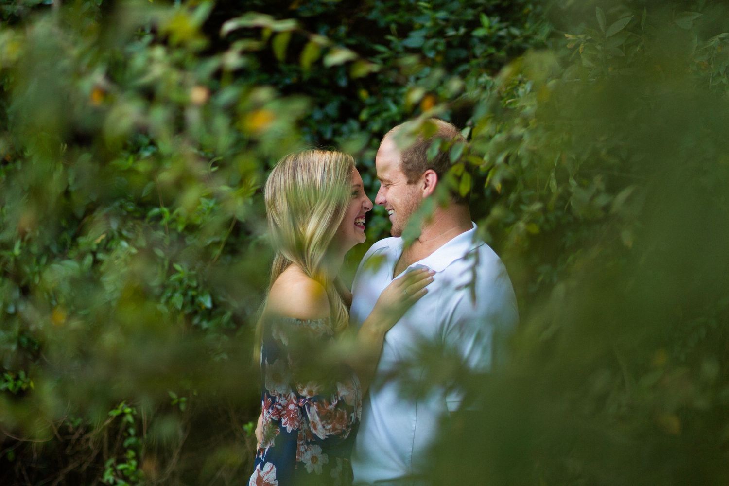 Intimate couple's portrait through green leaves during outdoor photo session.