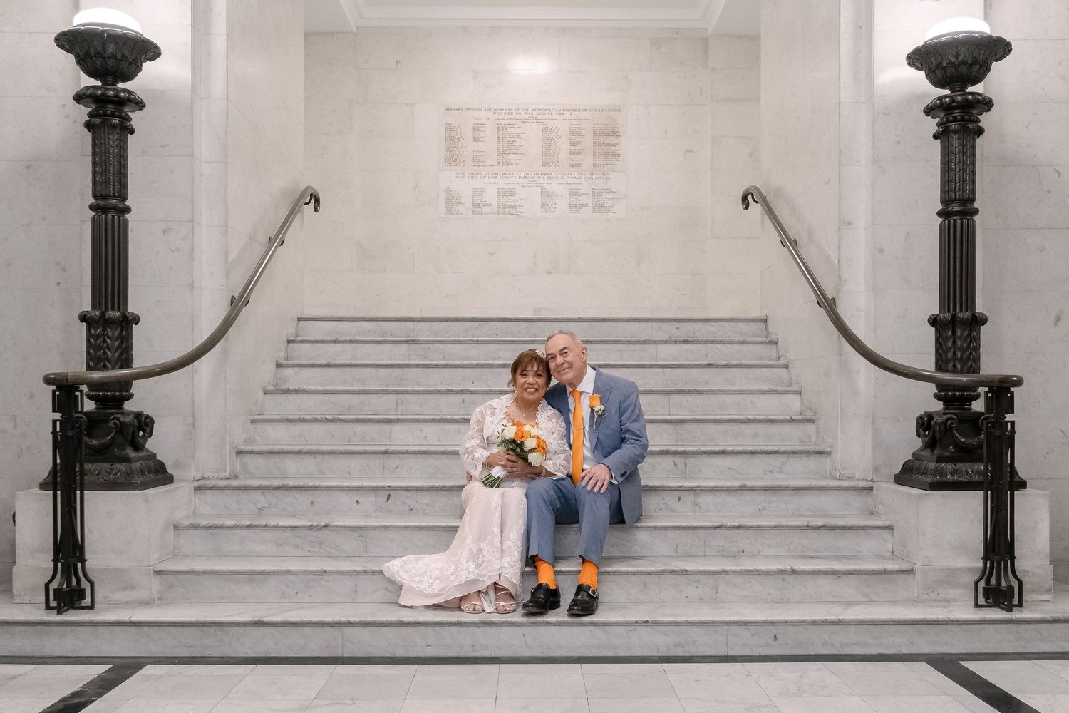Newlywed couple sit on the marble staircase of Old Marylebone Town Hall.