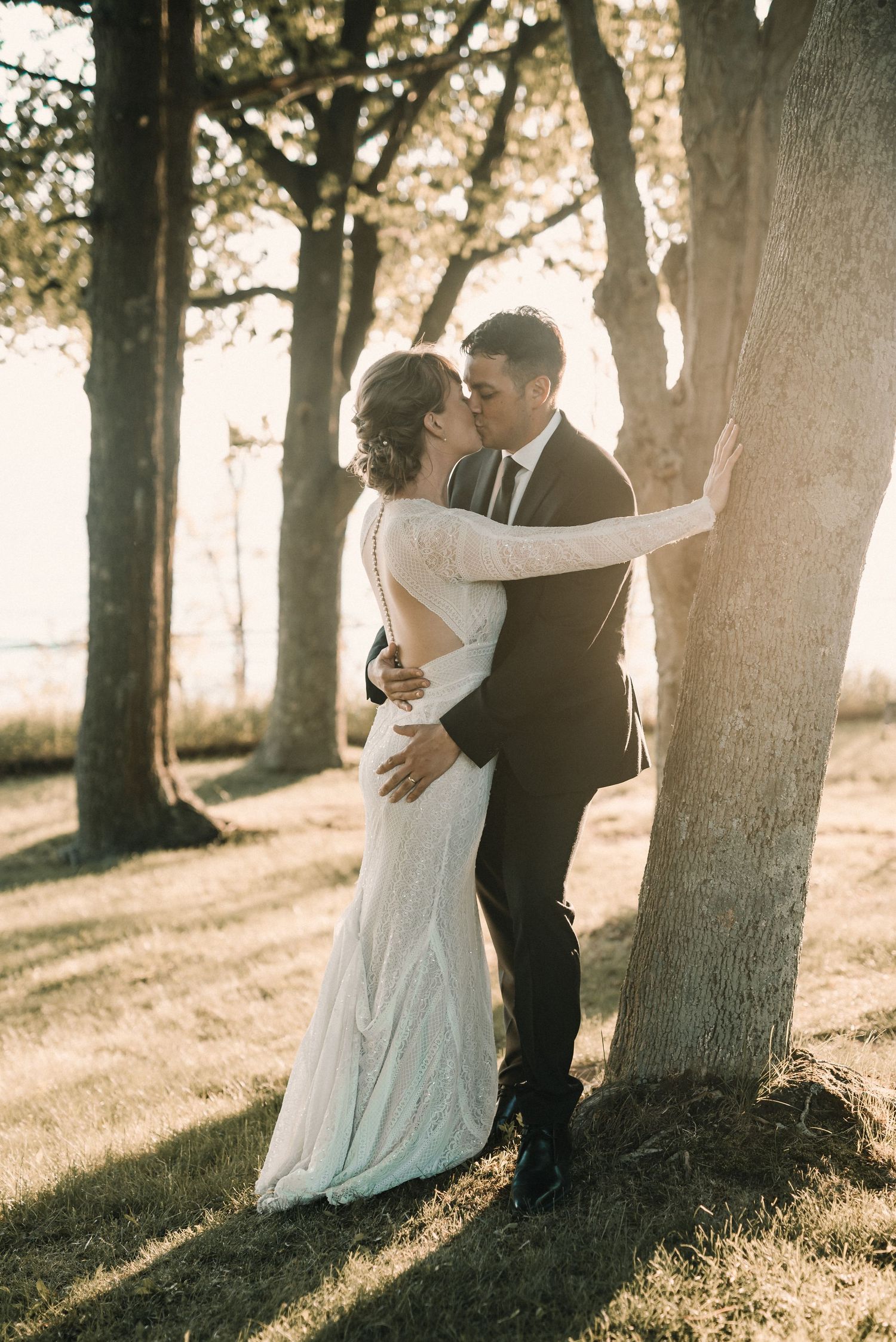 Sunlit wedding portrait against trees with golden afternoon light.