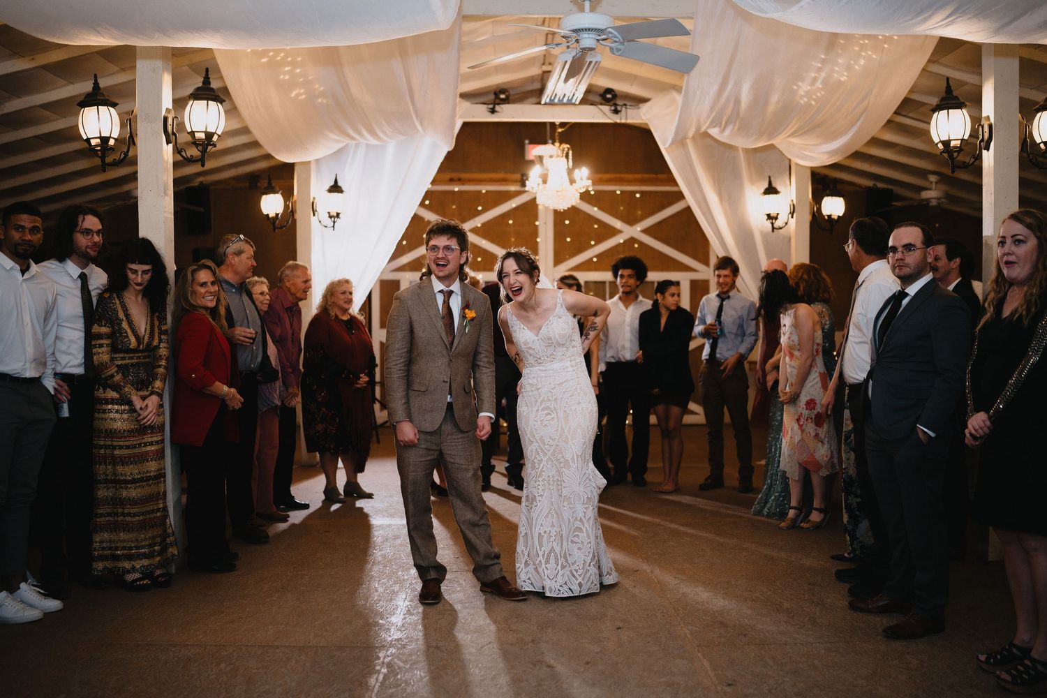 Bride and groom walk down the aisle together at a rustic indoor wedding venue with draped fabric and warm lighting.cinematic destination