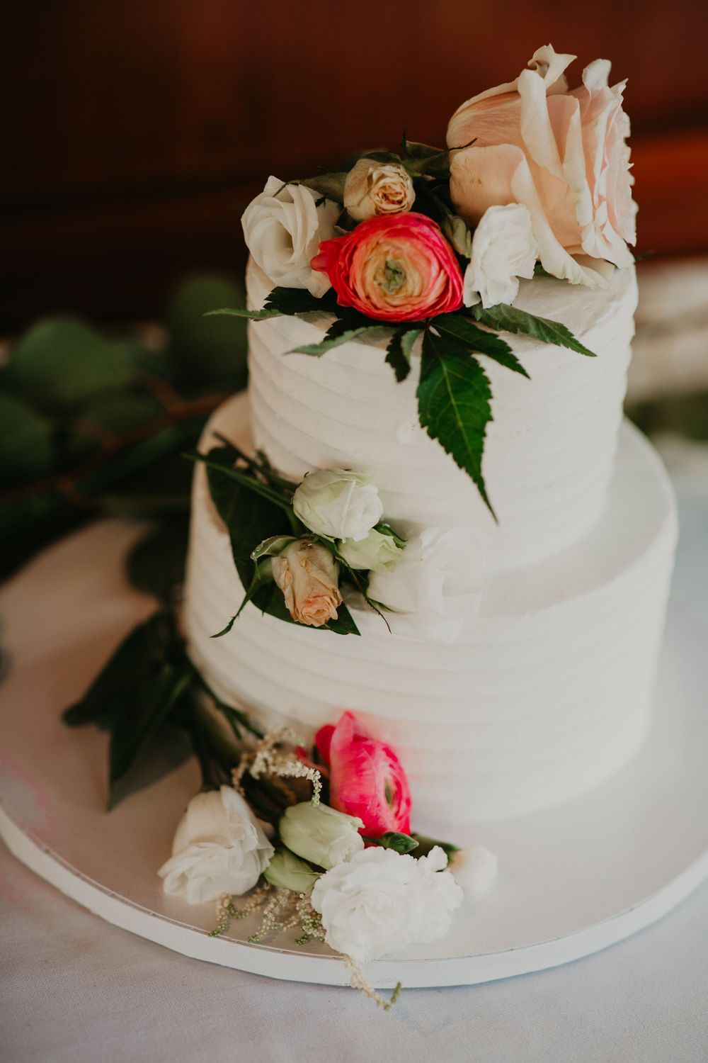 Elegant two-tier white wedding cake decorated with pink, red, and white fresh flowers.