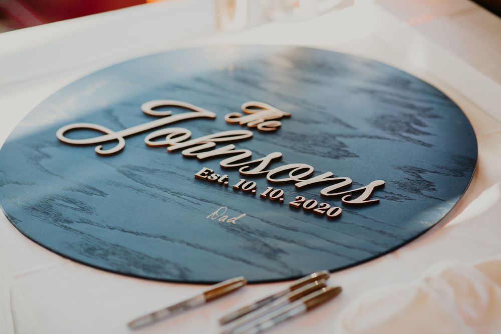 Personalized wooden wedding guest book sign reading The Johnsons Est. 10.10.2020 on a white table.