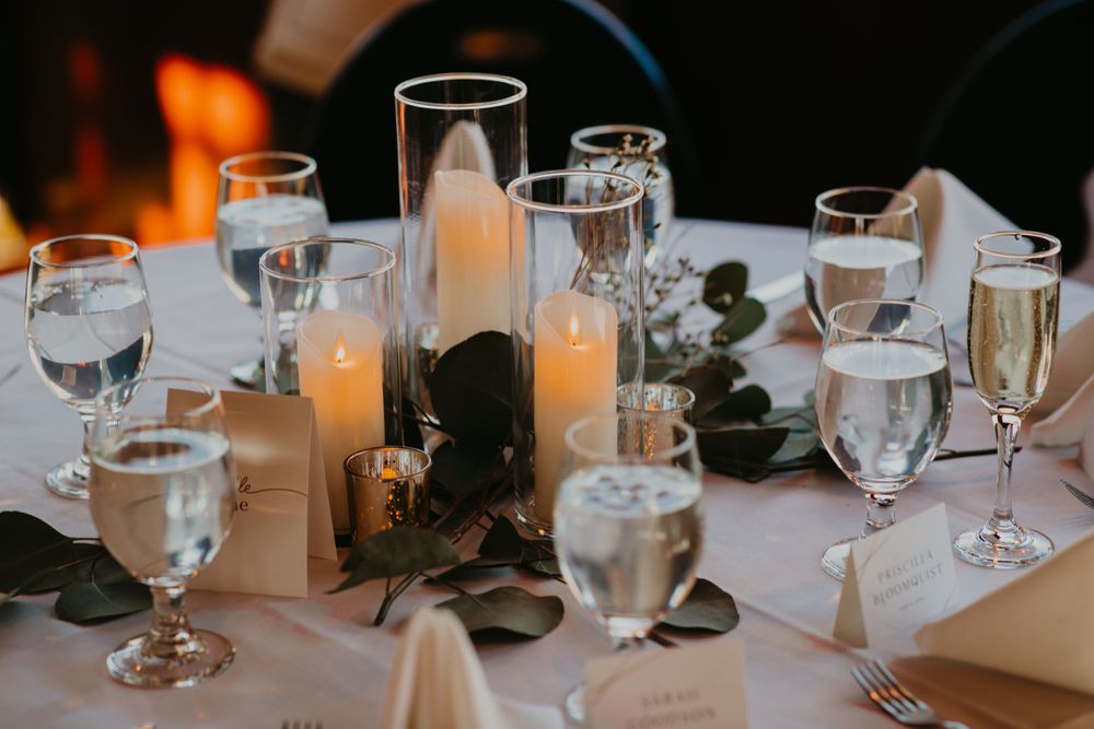 Elegant wedding reception table set with candles in glass holders, champagne flutes, and eucalyptus.