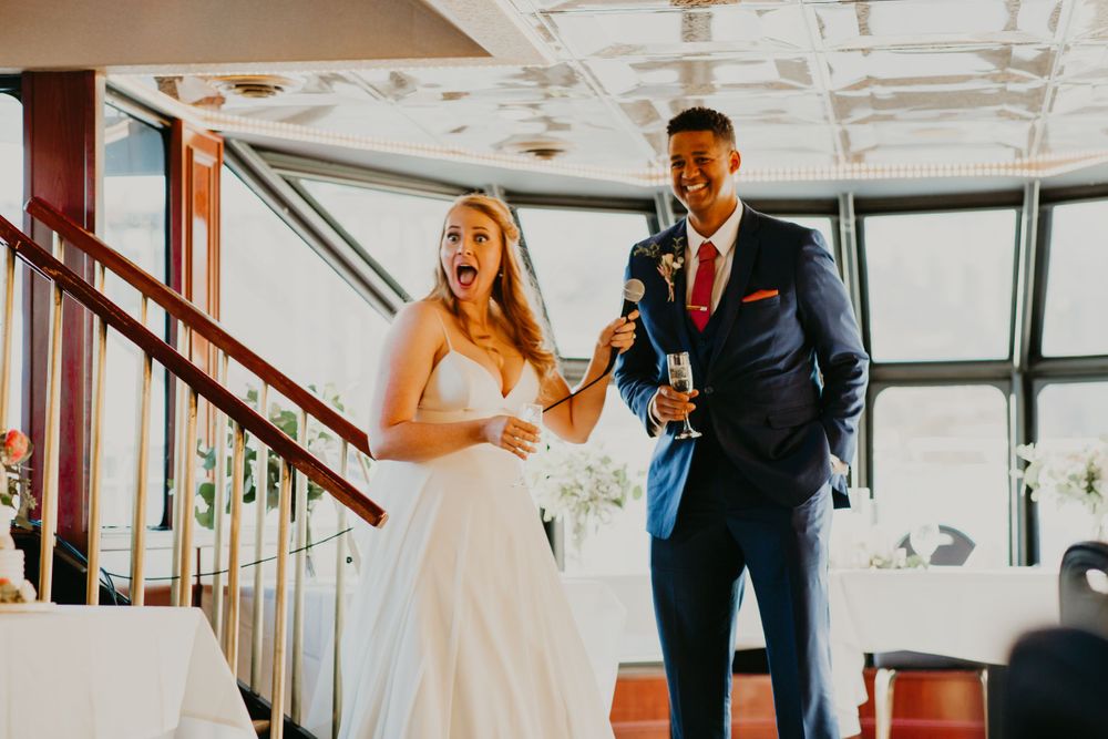 Bride and groom laughing and toasting with champagne during wedding reception speech on a boat venue.