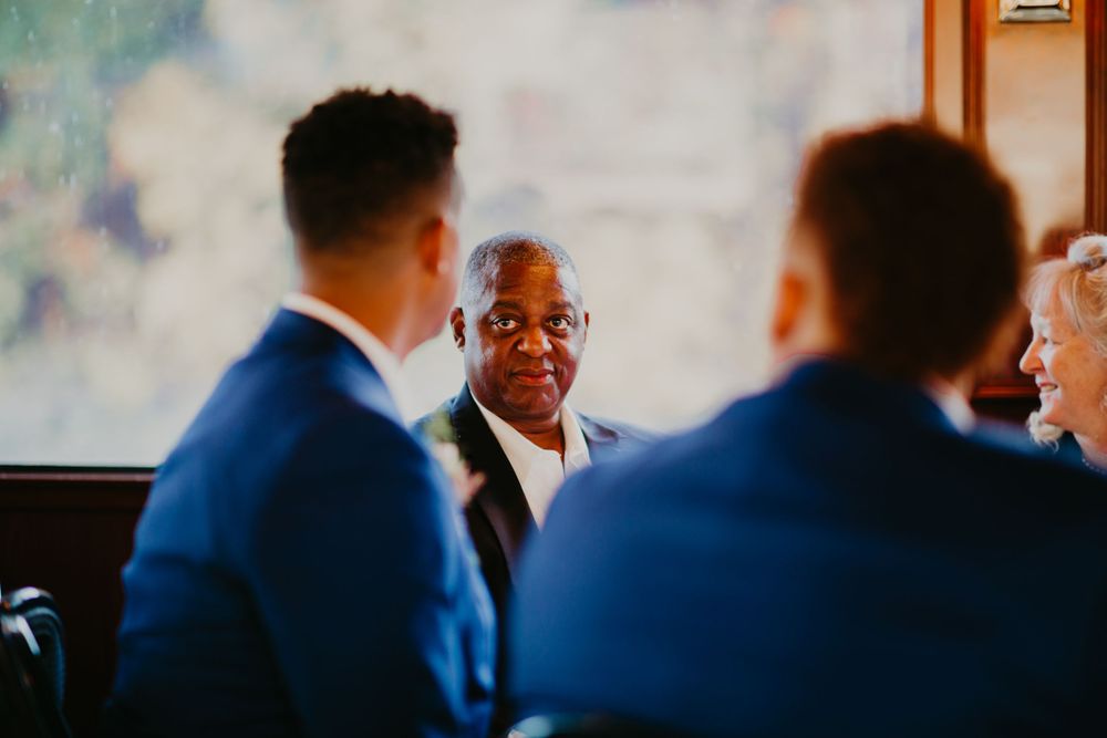 Older wedding guest conversing with groomsmen in blue suits at the reception.