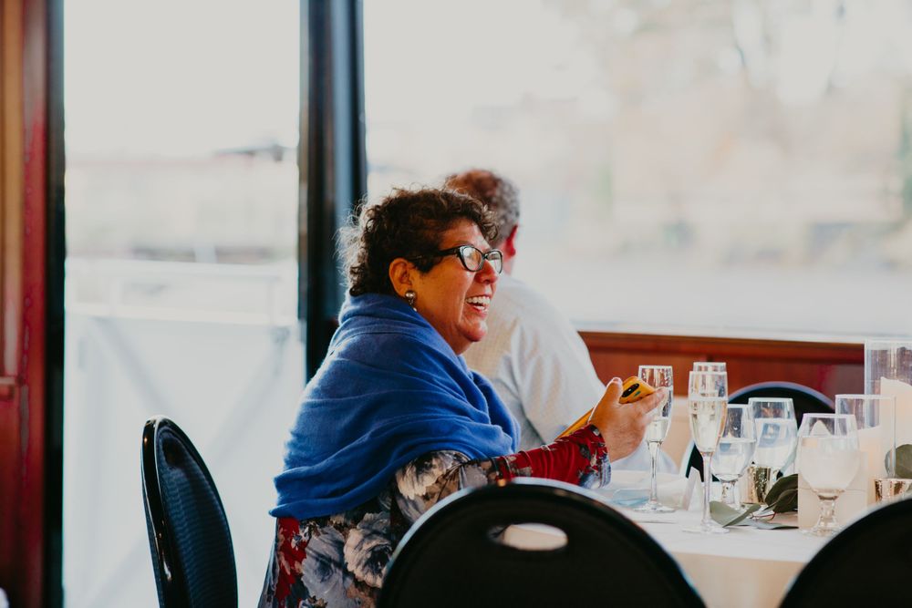 Wedding guest in a blue shawl smiles during a waterfront reception dinner.