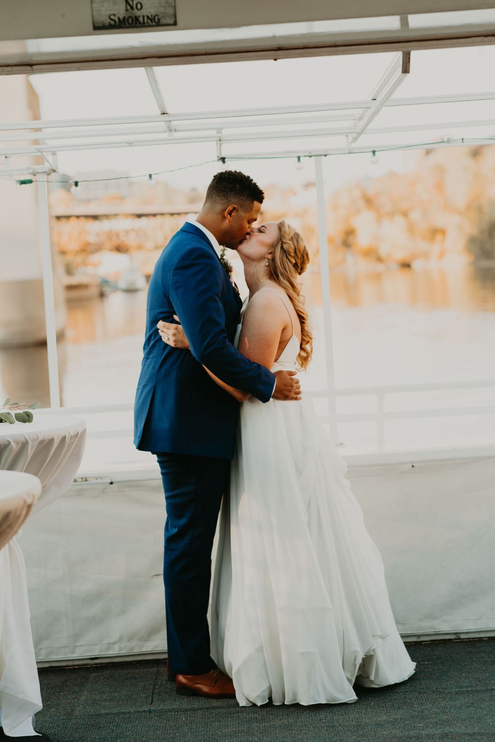 Bride and groom share their first kiss as a married couple at a waterfront wedding reception.