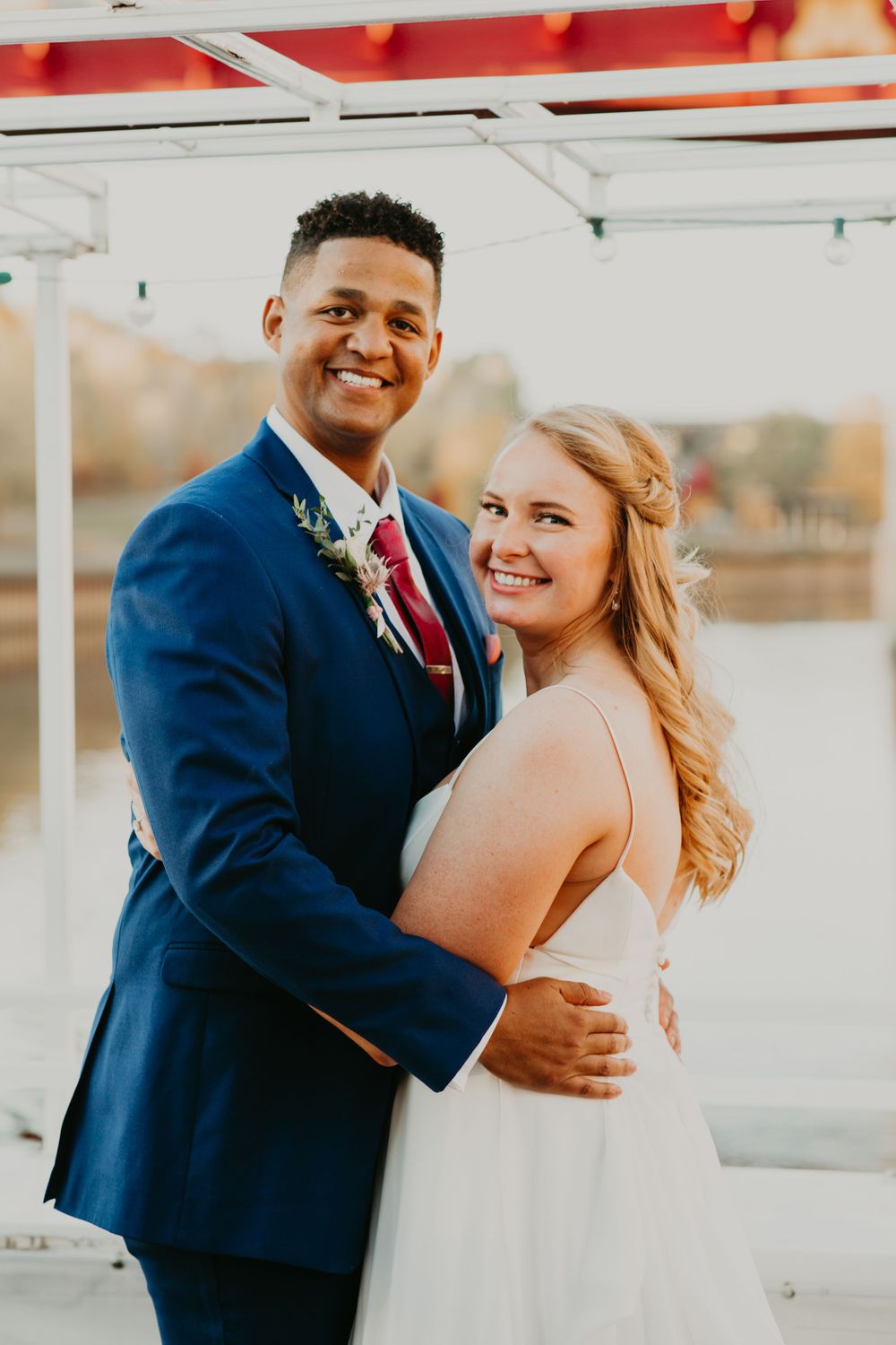 Smiling bride and groom pose together on a boat deck at their autumn wedding.