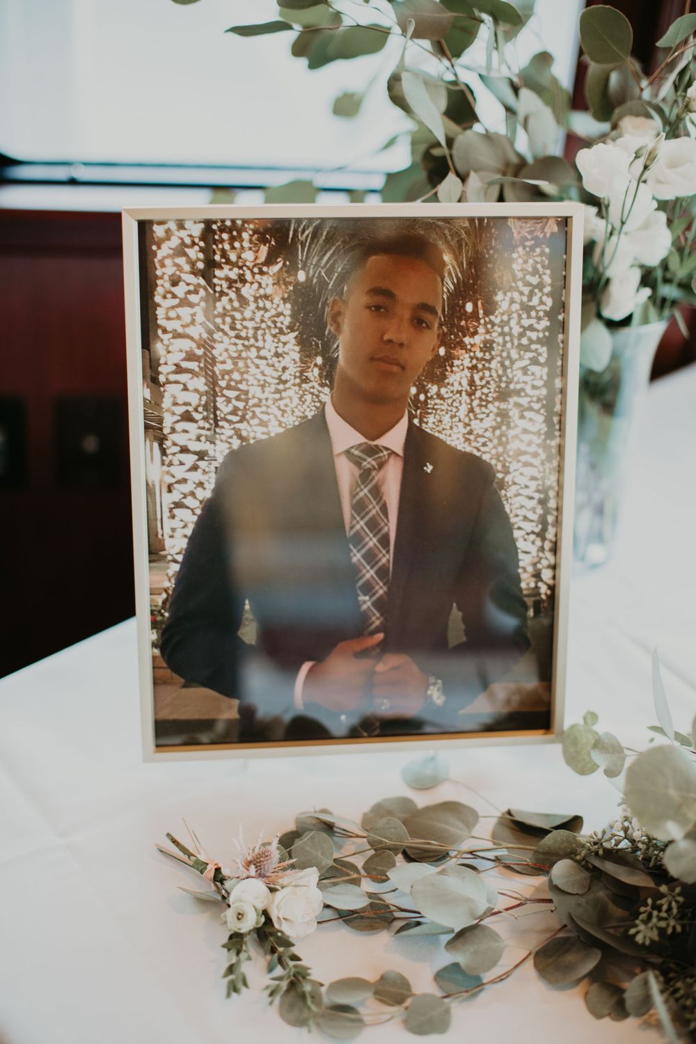 Framed memorial photo of a young man displayed with a floral wreath at a wedding.