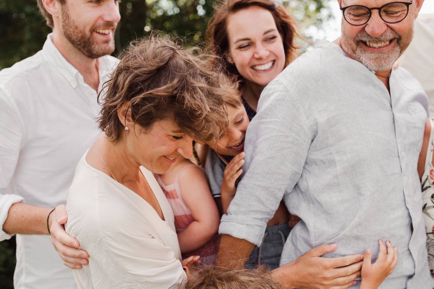 A group embraces while laughing together outdoors on a sunny day.