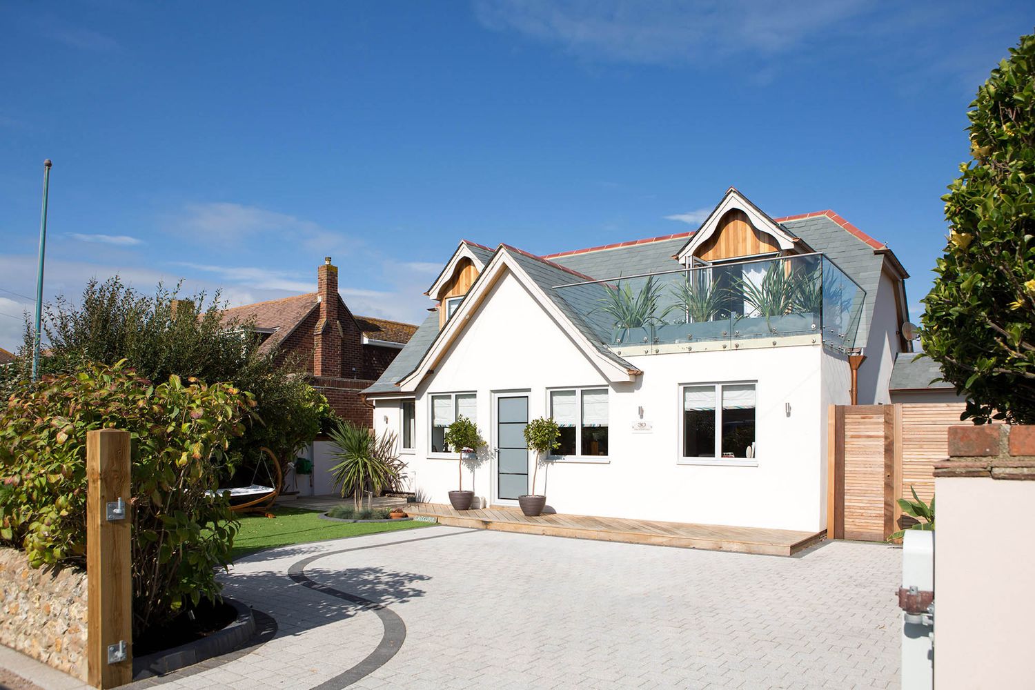 Modern white house exterior with glass balcony and contemporary architectural details on a sunny day.
