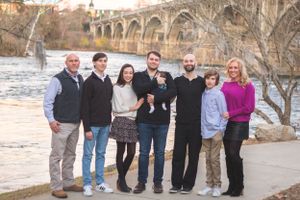 Family group photo with seven people standing by a river with an arched bridge in the background.