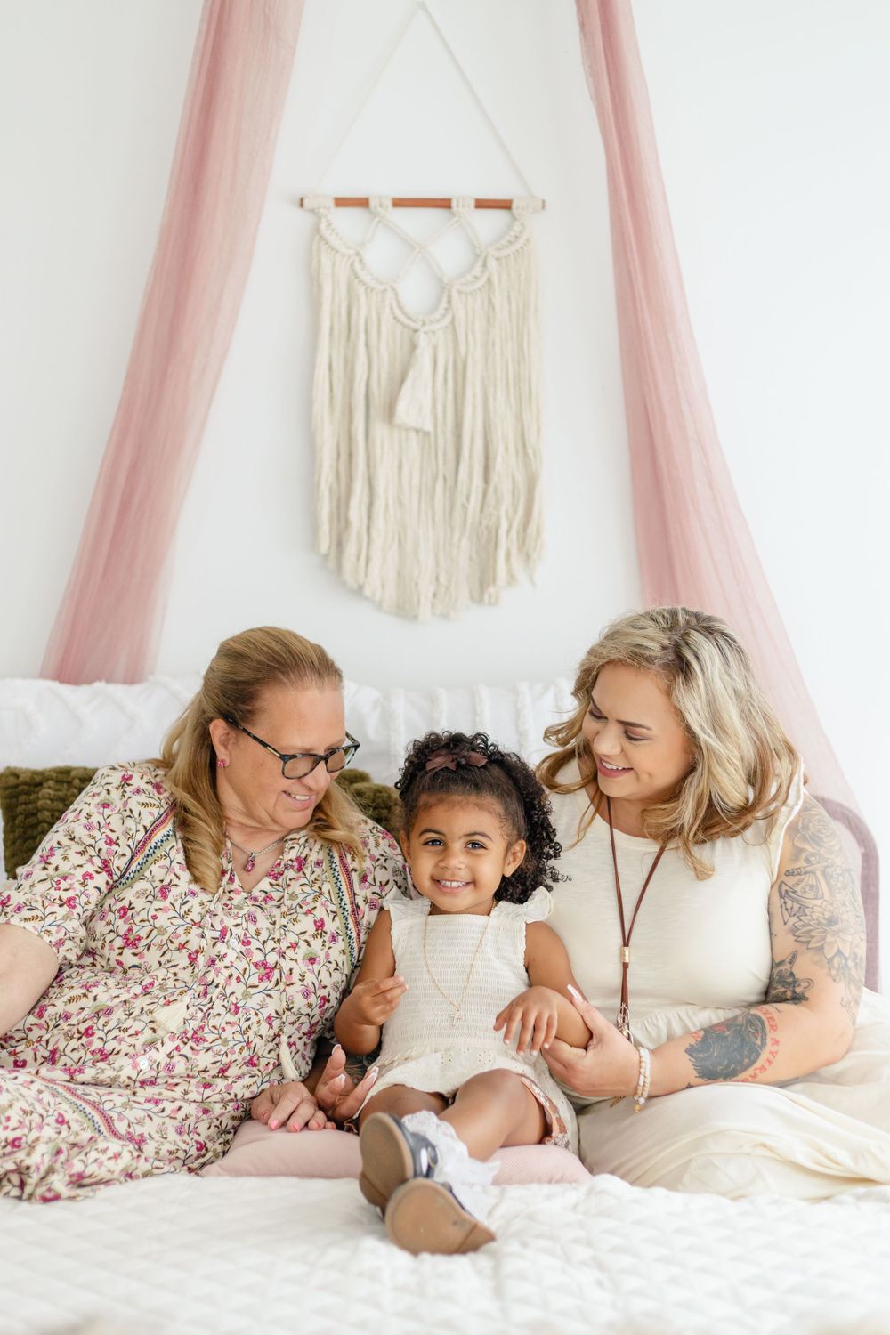 Family photo session in cozy bedroom setting with macrame wall decor and pink accents.