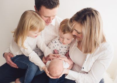 An intimate family portrait showing parents and children gathered around a newborn baby.