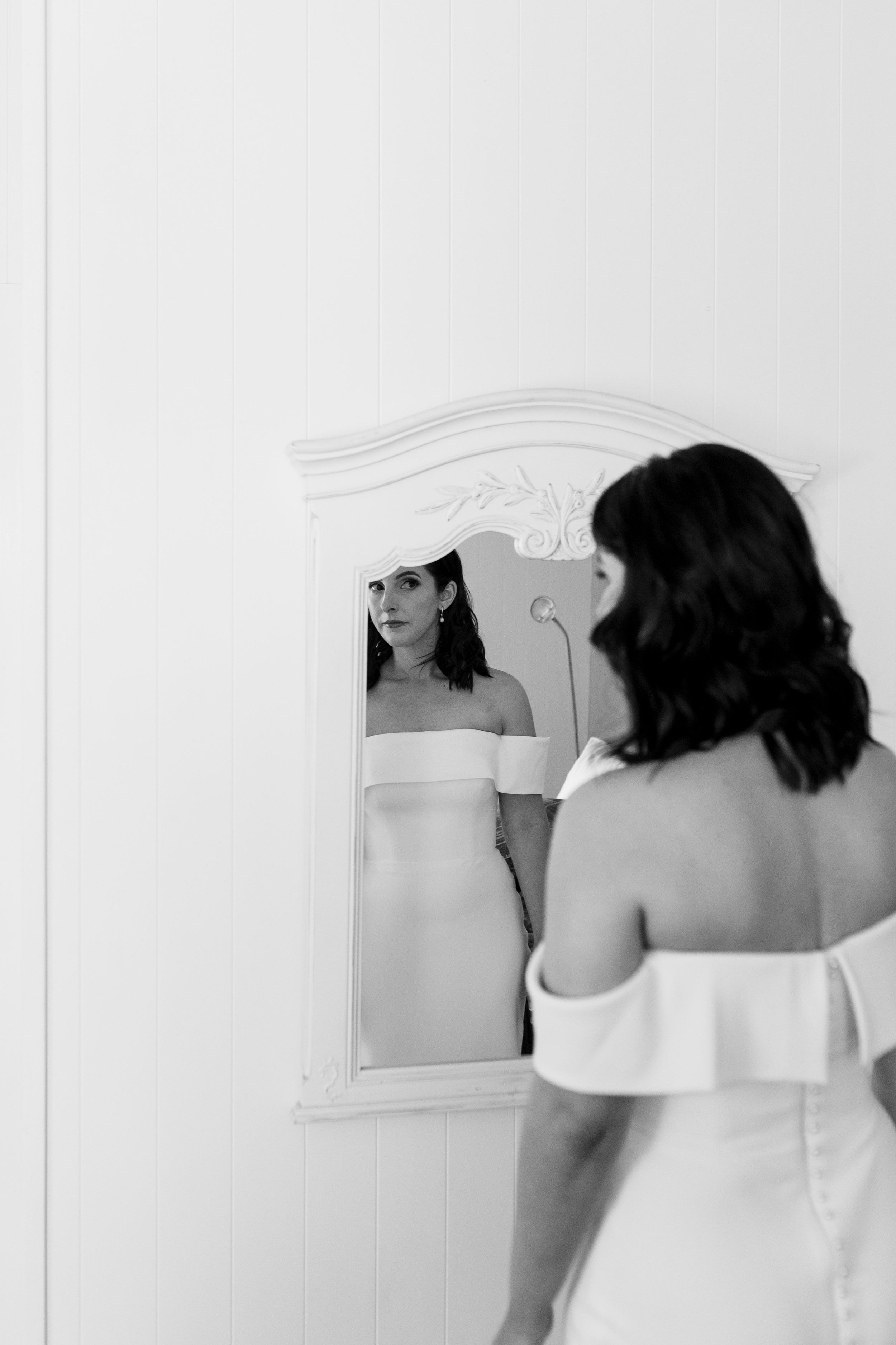 A black and white photo of someone looking at their reflection in an ornate white mirror.