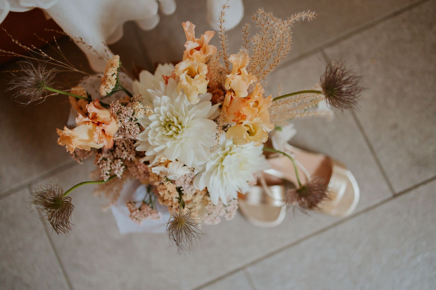 Floral arrangement with white and peach blooms placed on a tiled floor.