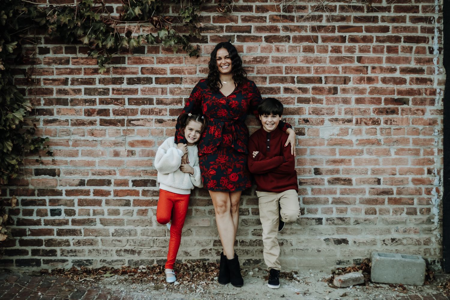 Family photo session against rustic brick wall with red plaid accents.
