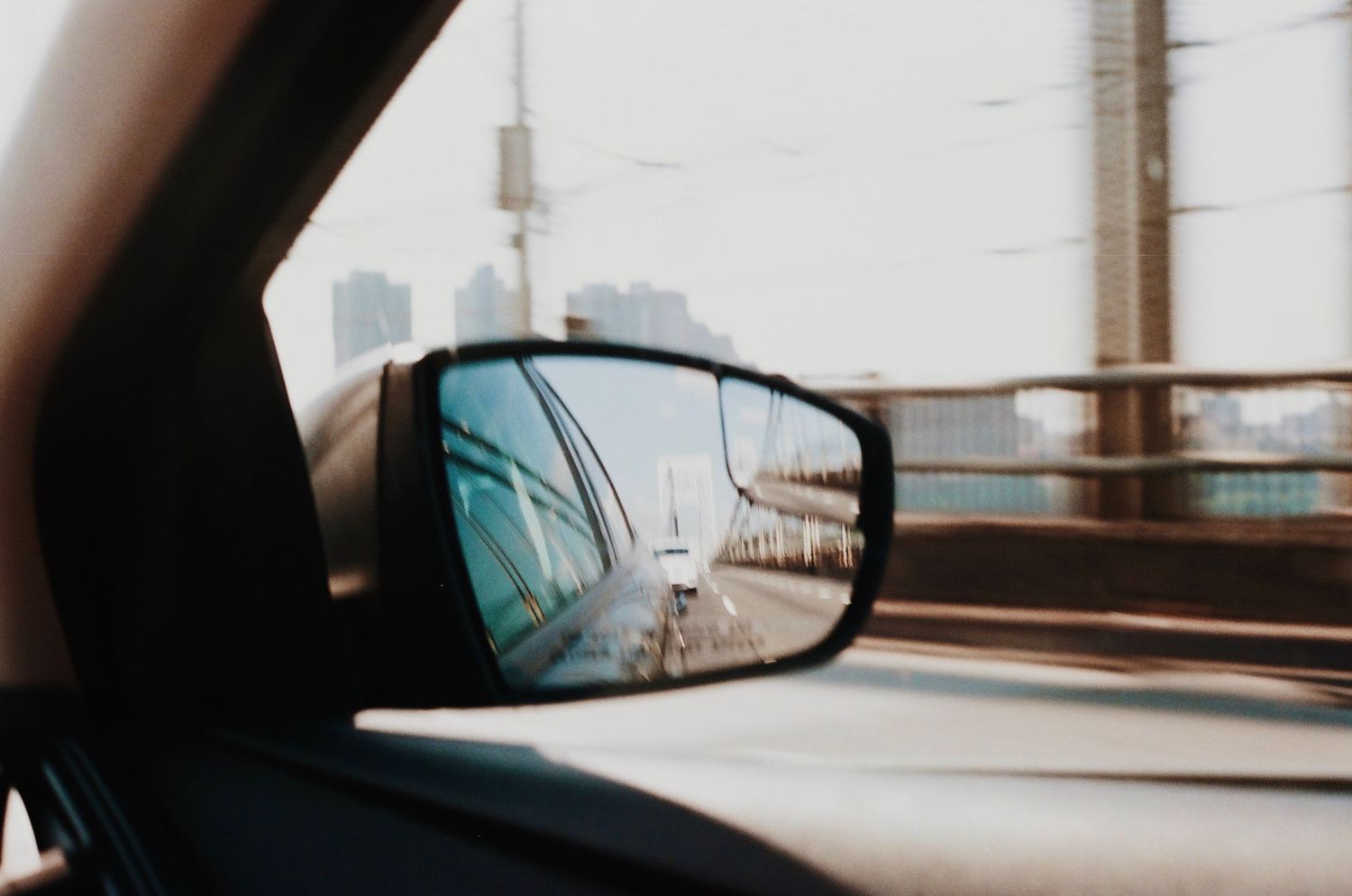 Car side mirror reflection showing urban scenery and utility poles during daytime.
