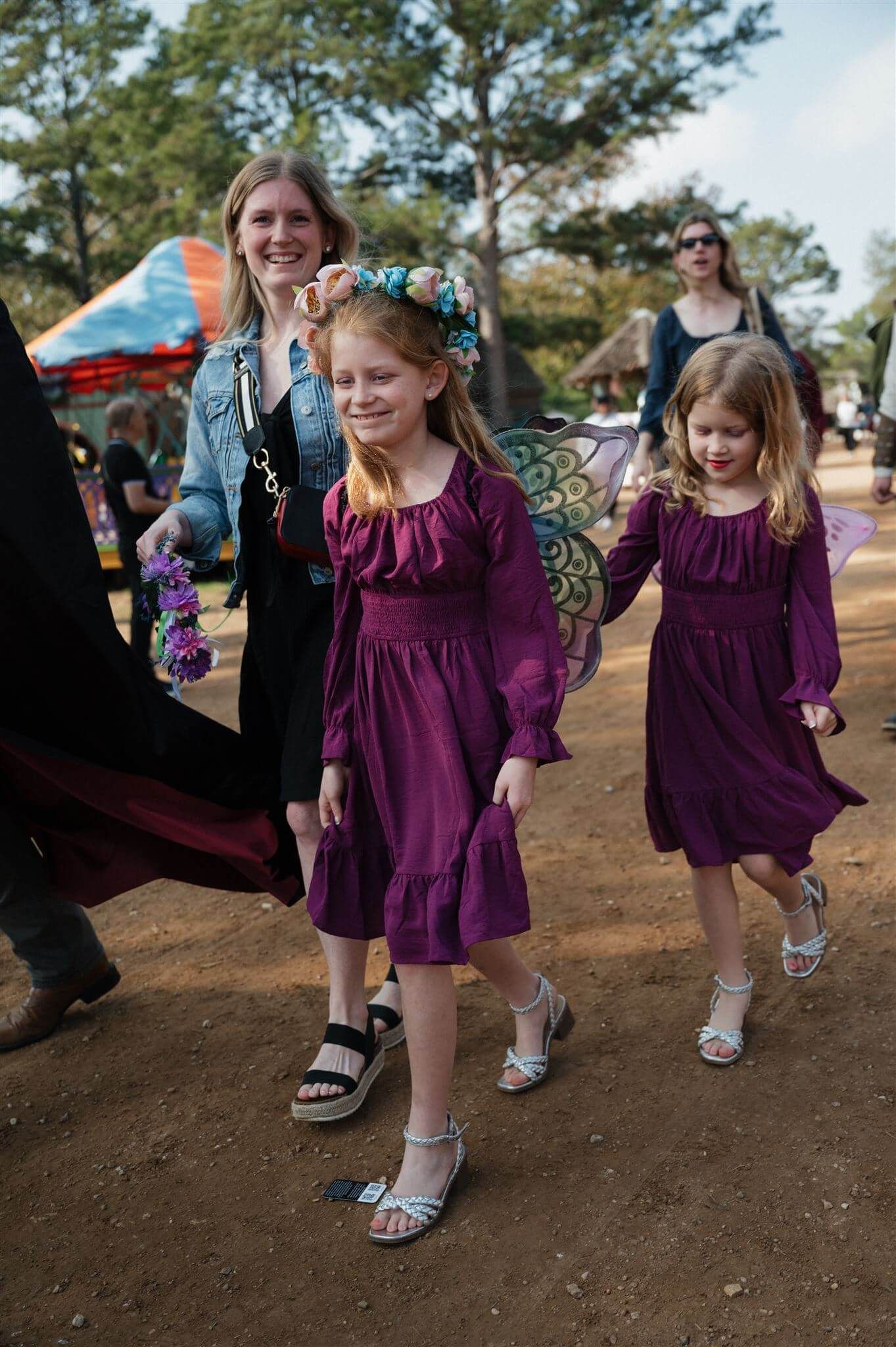 Several attendees in purple dresses walk together at a renaissance fair on a sunny day.