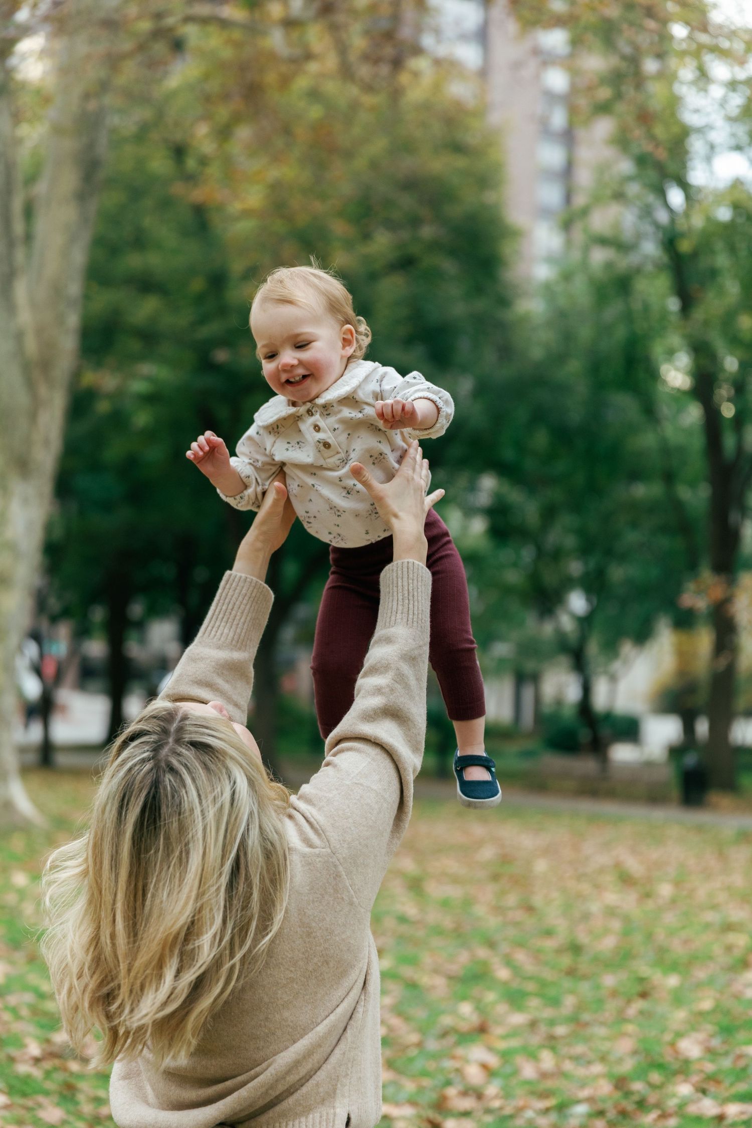 Parent lifting toddler in the air during playful moment at autumn park.