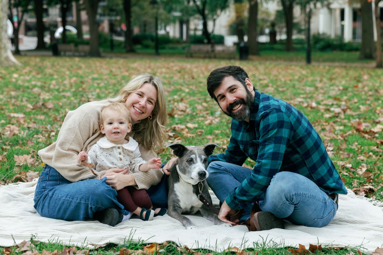 Family sitting on blanket with their dog in a park during autumn.
