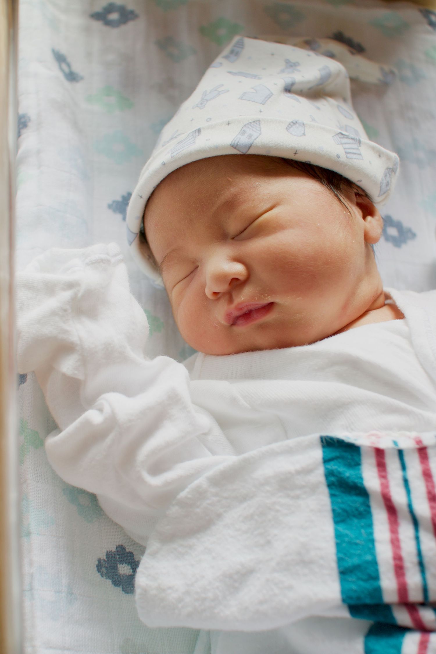 A peaceful sleeping newborn wearing a patterned hat and striped outfit.