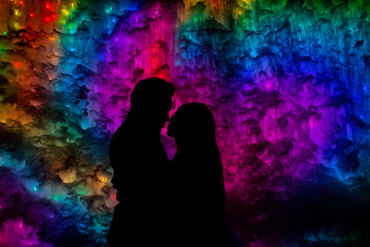 Silhouettes against vibrant rainbow colored background creating romantic scene.
