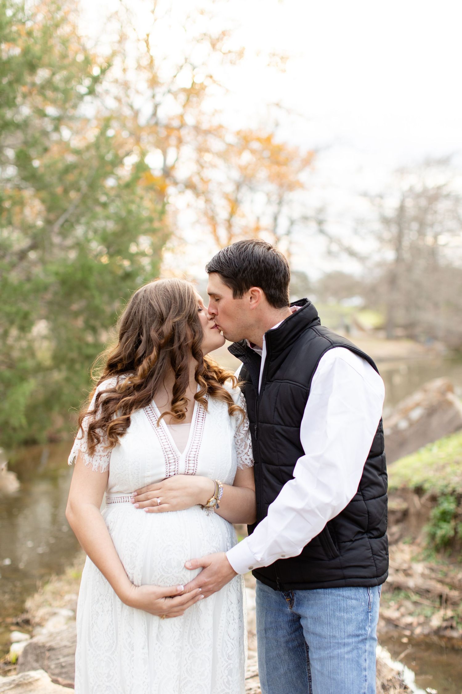 An intimate maternity photo of a couple by a stream with fall foliage.