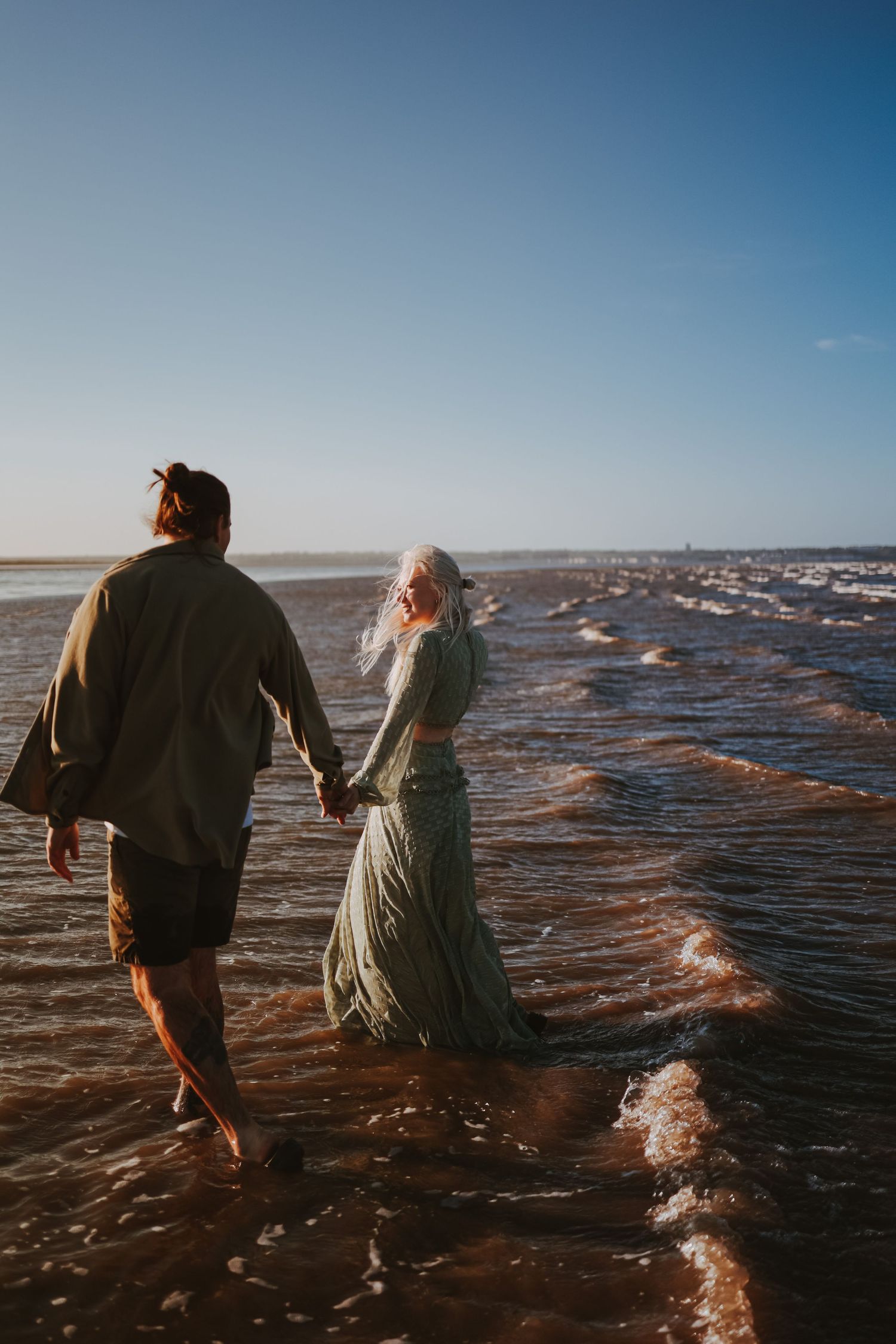 Two people wade through shallow ocean waters at sunset.