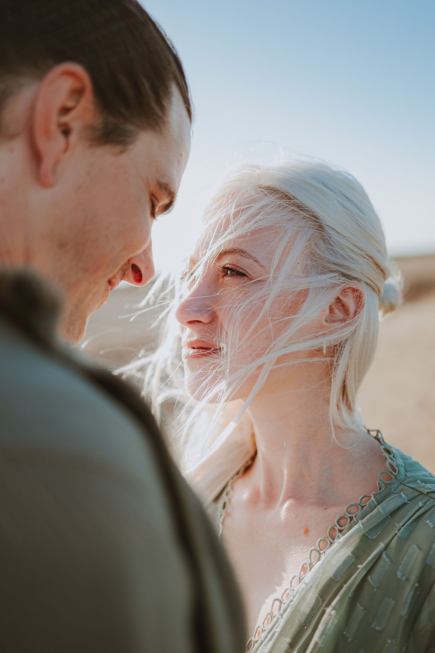 A couple shares an intimate moment on a sunny beach with soft lighting.