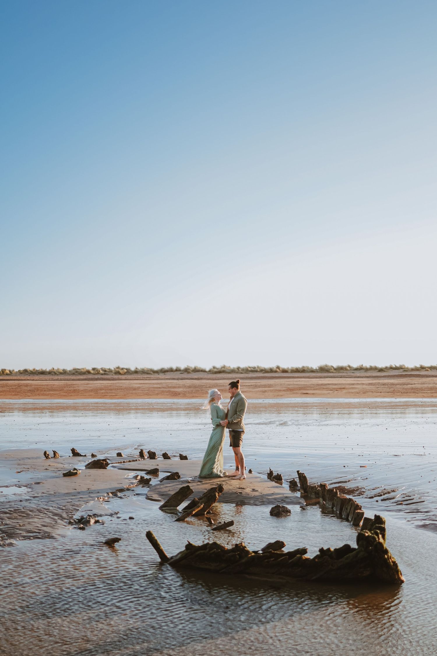 An old shipwreck rests on a vast beach during low tide.