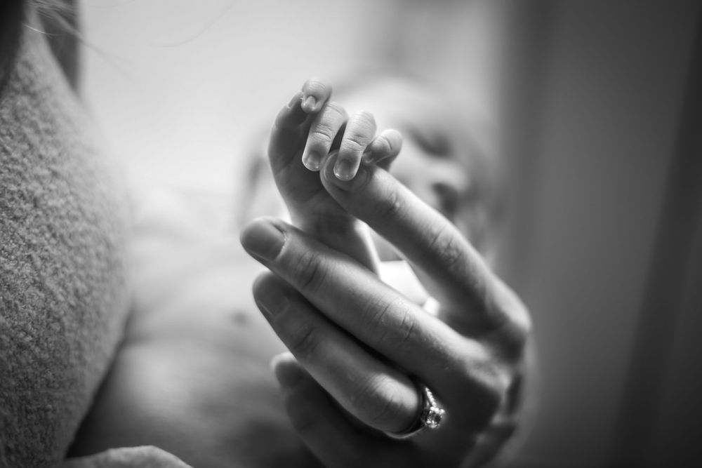 A newborn baby grabs their mother's finger in candid black and white in-home portrait