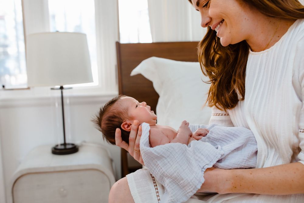 A new mom smiles at her newborn baby in neutral colors in home portrait