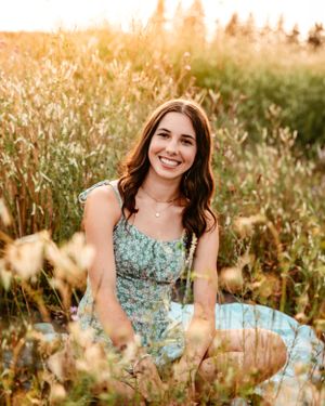 Summer portrait of woman in floral dress sitting among tall golden grass at sunset.