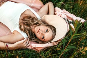 Dreamy outdoor portrait of woman lying in grass wearing white tank top.